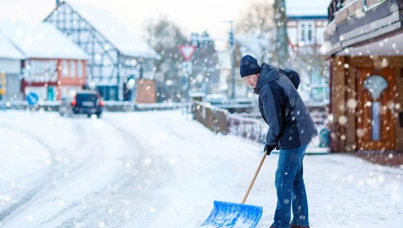 Man with snow shovel cleans sidewalks in winter. Winter time in Europe. Young man in warm winter clothes